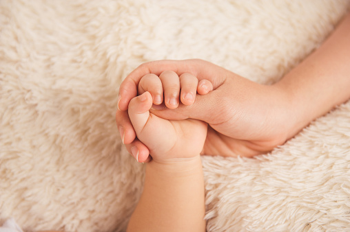 Mom holding baby hand isolated on white blanket