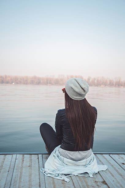 istock Girl sitting on pier and lookingat the river 473626228