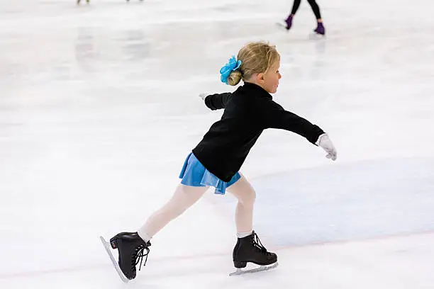 Cute young girl practicing figure skating on indoor ice skating rink.