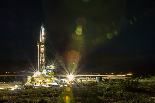 BFracking Rightly lit drilling Fracking Rig in a town at night with star trails above Fracking Oil Well is conducting a fracking procedure to release trapped crude oil and natural gas to be refined and used as energy