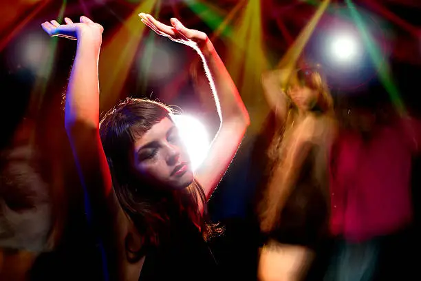 Photo of an intoxicated female dancing at a nightclub and high on drugs or drunk on alcohol.  She has her hands up like she is dancing in a rave or party and looks disheveled.  Her make up is smeared like a junkie.  She is either a drug addict or an alcoholic.  