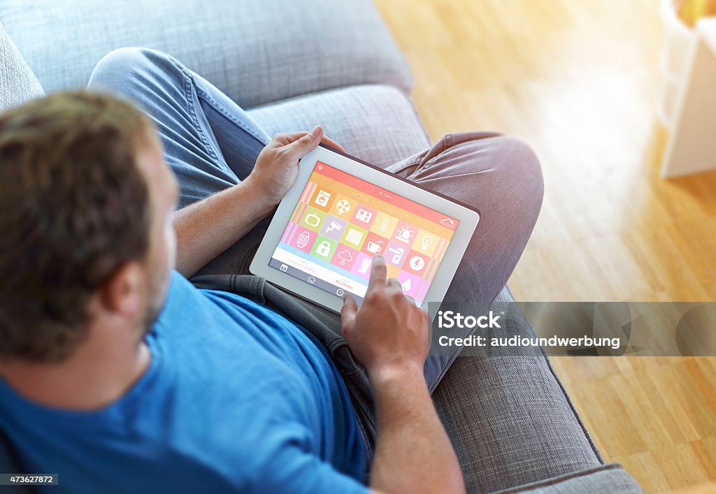 Smart Home Device - Home Control smart house, home automation, device with app icons. Man uses his tablet PC with smarthome app to control his house. the new generation of the internet of things. 2015 Stock Photo