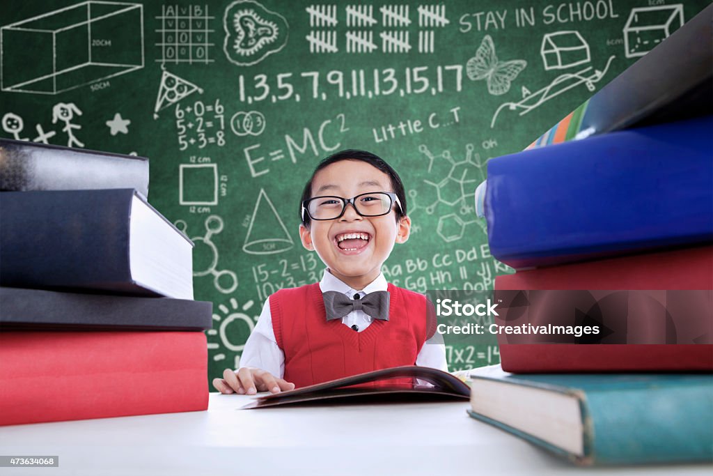 Asian boy laughing in class with stack of books Close-up of Asian boy laughing in class with stack of books Child Stock Photo