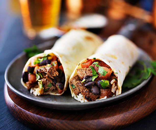 two mexican steak burritos with beer mexican beef burritos with beer in background burrito stock pictures, royalty-free photos & images