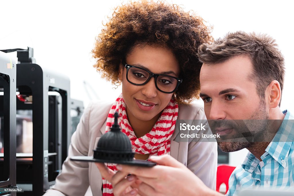 Woman and man in 3D printer office Two business colleagues - afro american woman and caucasian man, working together in a 3d printer office, watching 3d printout. 3D Printing Stock Photo
