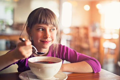 Beautiful smiling little girl eating a soup. Soft focus. The soup is traditional polish red beetroot soup.