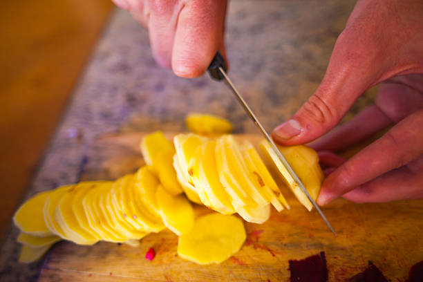 istock Young Slicing Russet Potatoes in Kitchen at Home 473675476