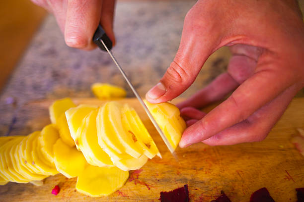 istock Young Slicing Russet Potatoes in Kitchen at Home 473675482
