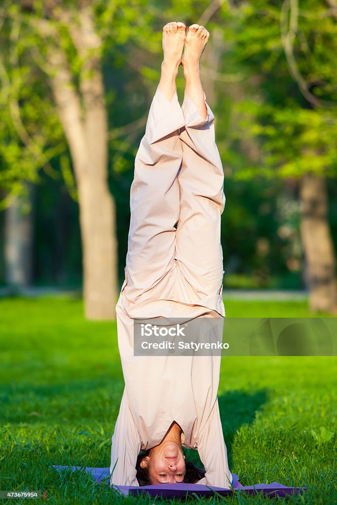 Practicing yoga in the morning, with trees  background Yoga utthita trikonasana triangle pose by woman in white costume on green grass in the park around pine trees 2015 Stock Photo