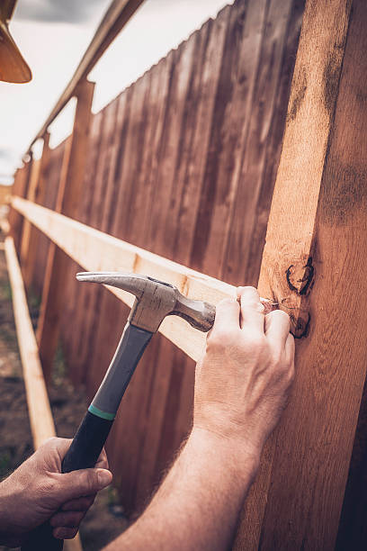 istock Construction worker hammering nail into fence framework. New construction. Fences. 473678160
