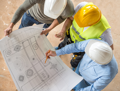 Group of civil engineers looking at blueprints at a construction site and wearing helmets