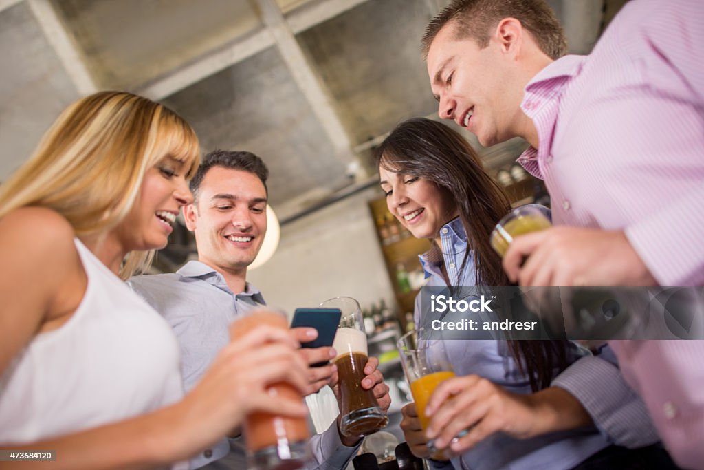 Friends on a night out social networking Group of friends having drinks on a night out and social networking on a cell phone 2015 Stock Photo