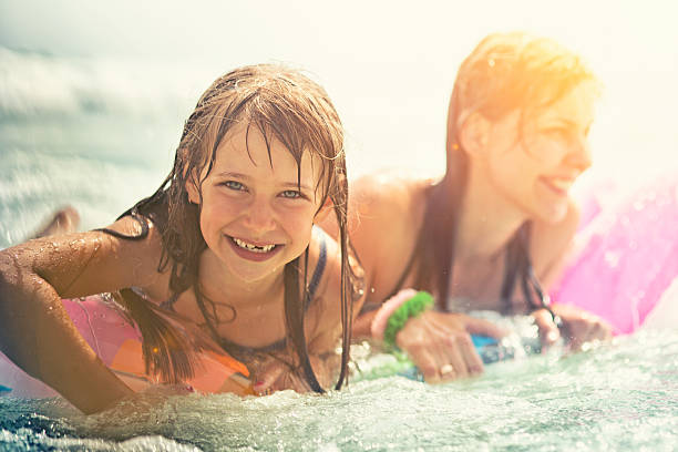 Cute little girl learning to swim with mother in pool in sunset