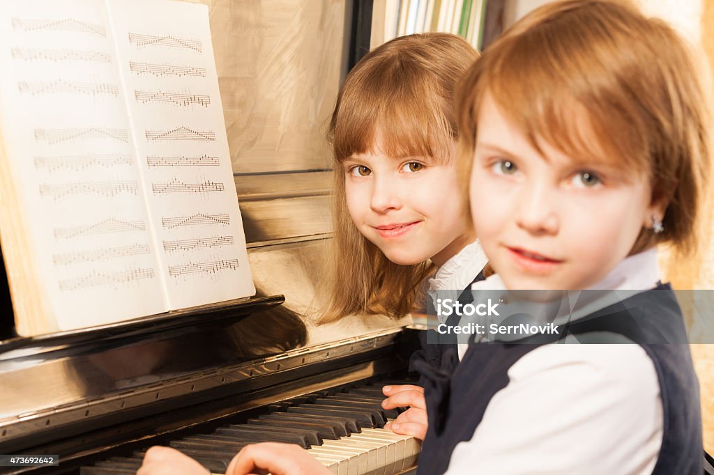 Smiling beautiful small girls playing piano Smiling beautiful small girls playing piano together with notes during lesson 2015 Stock Photo