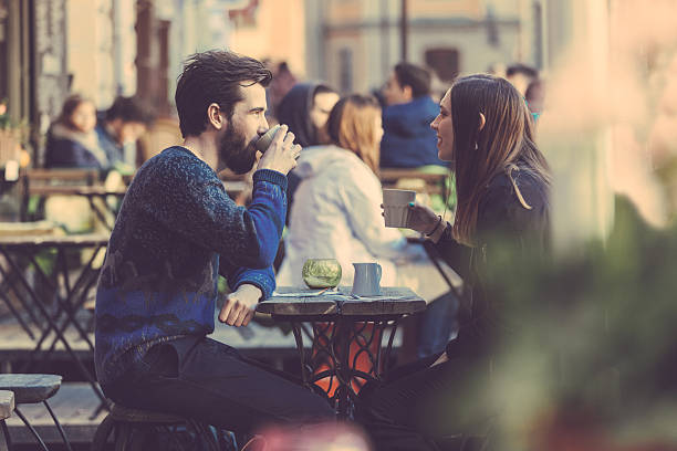 Hipster couple drinking coffee in Stockholm old town. They're sitting face to face. The man is wearing a blue sweater and the woman a striped shirt with black leather jacket.