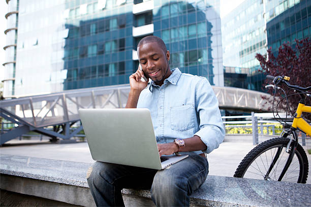 Businessman seated outside with computer and on phone