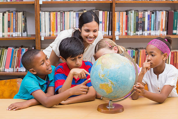 istock Cute pupils and teacher looking at globe in library 473706510