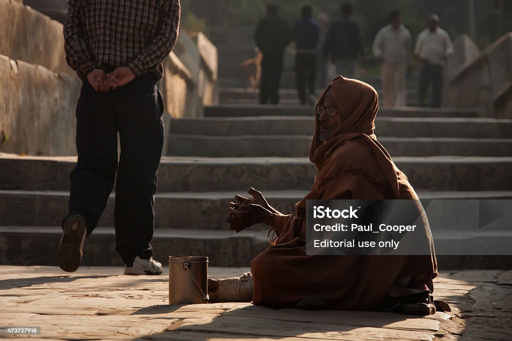 Beggar at the Pashupatinath Temple, Kathmandu, Nepal. Kathmandu, Nepal - November 9, 2012: Woman sitting on the temple steps at Pashupatinath Temple begging for money in the morning sunlight, as worshipers and pilgrims pass her by. 2015 Stock Photo