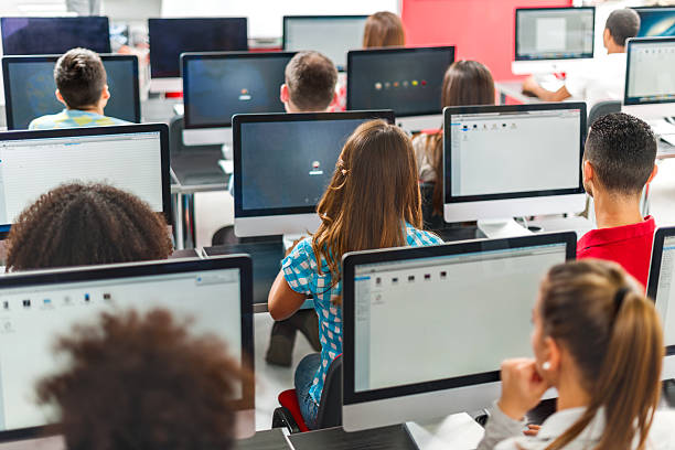 Rear view of group of people in a computer seminar. Rear view of large group of people sitting at a computer class and using computers. computer lab stock pictures, royalty-free photos & images