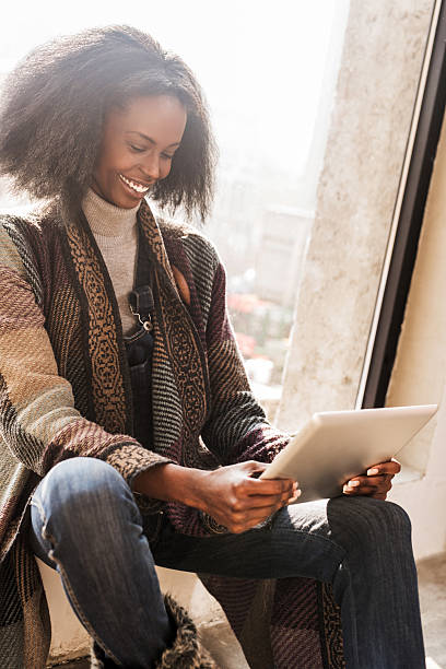 istock Smiling African American woman using touchpad by the window. 473738144