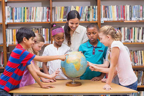 istock Cute pupils and teacher looking at globe in library 473742212
