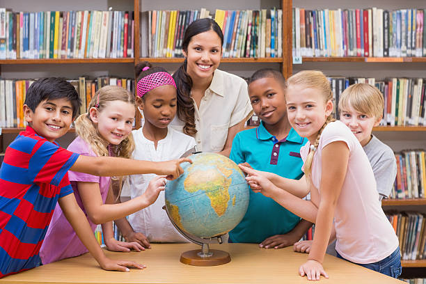 istock Cute pupils and teacher looking at globe in library 473742218