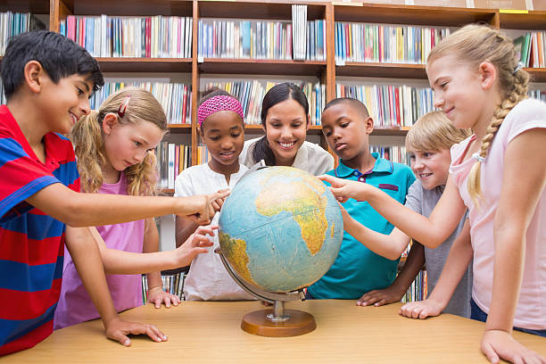 istock Cute pupils and teacher looking at globe in library 473742220