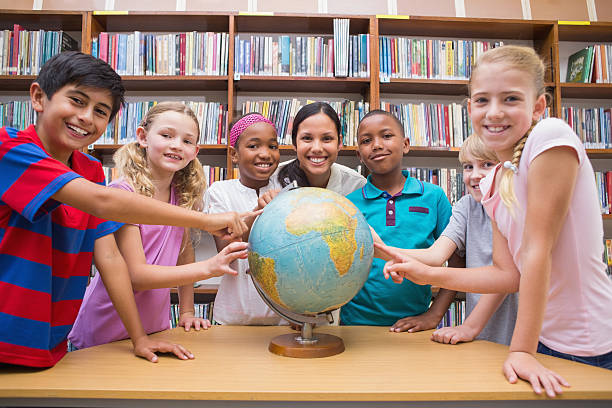 istock Cute pupils and teacher looking at globe in library 473742224