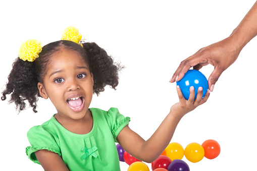 Portrait of adorable four year old african american girl. She has pigtails with bright yellow hair bows in them.Her mouth is wide open. She is being given blue plastic ball and others are in back of her.  Shot from chest up taken with a Canon 5D Mark 3 . rm