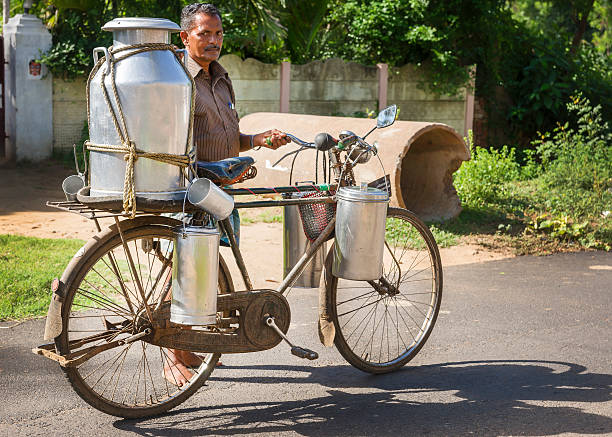 Kumbakonam, India - October 13, 2013:  Milkman carrying a very large and small milk cans on his rusty bike along a rural road.