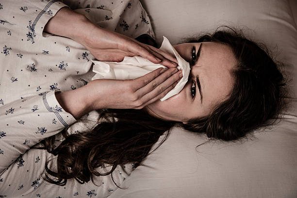 istock Woman with flu and feaver lying in bed blowing nose 473747110