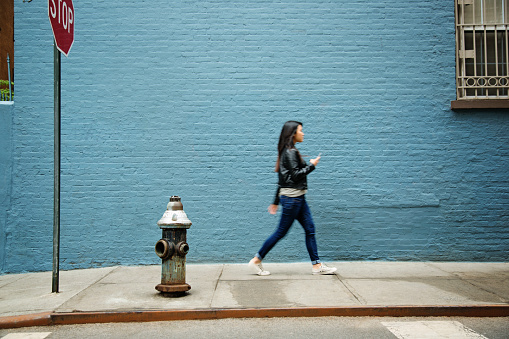 Young woman walking with mobile phone. Sharpness on wall. 