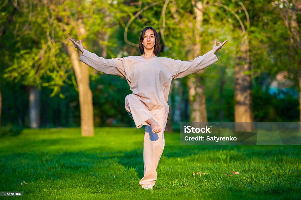 Practicing yoga in the morning, with trees  background Yoga utthita trikonasana triangle pose by woman in white costume on green grass in the park around pine trees 2015 Stock Photo