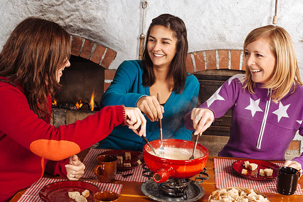 Photo of three beautiful females dipping bread into the melted cheese in a fondue pot.