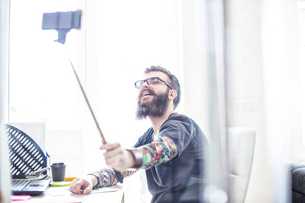 istock Tattooed hipster taking selfies in office with selfie stick 473786078
