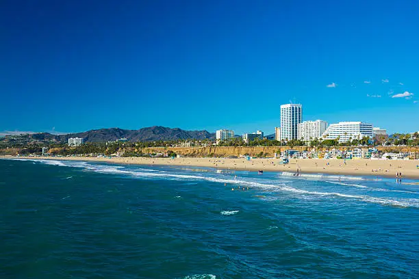 Santa Monica downtown skyline, beach (with waves), houses, and the Santa Monica mountains in the background.