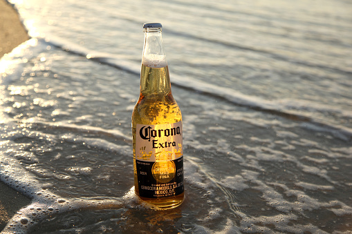 Virginia Beach, Va. USA  - May 15, 2015: Corona Extra Beer produced in Cervecería Modelo made in Mexico as the bottle stands on the beach the tide rolls in over the bottle showing it's refreshment especially in the summer heat.