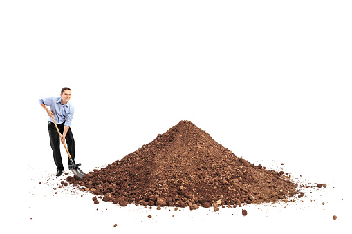 Cheerful young man shoveling a big pile of dirt and looking at the camera isolated on white background