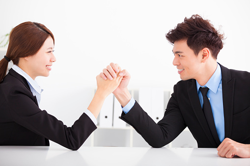 Business man and woman arm wrestling on desk in office