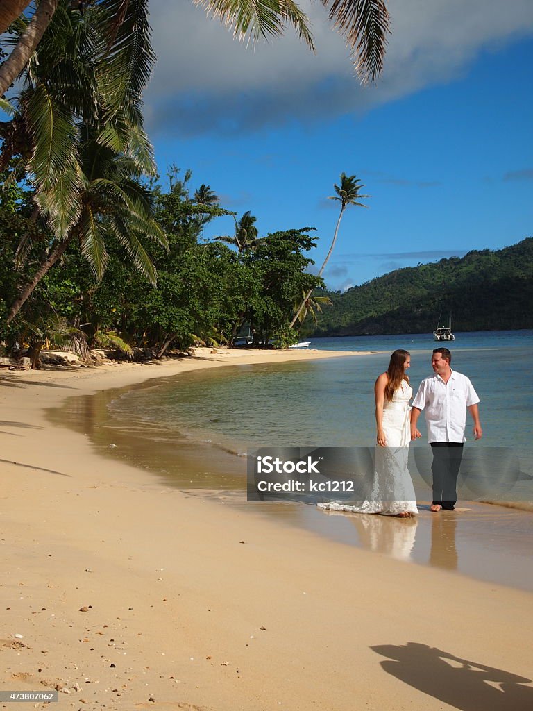 Bride & Groom Holding Hands Walking The Beach in Fiji A newly-wed couple walks along the shore of the South Pacific Ocean on an island in Fiji while shooting a "trash the dress" photoshoot while on their honeymoon. Destination Wedding Stock Photo