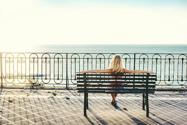 istock Woman sitting on a bench and looking at sea 473819026