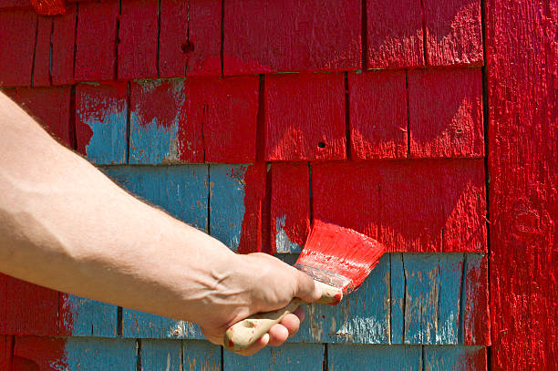 istock Man's hand and brush painting red on old shingles. 473830400