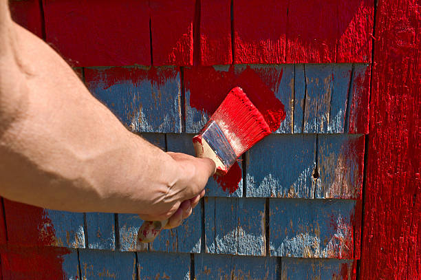 istock Man's hand and brush painting red on old shingles. 473830408