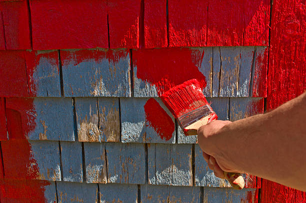 istock Man's hand and brush painting red on old shingles. 473830416