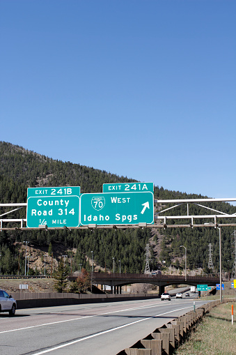 Idaho Springs, CO, USA - April 23, 2014: Two signs giving notice of exits in Idaho Springs with vehicles traveling on the highway during the day.