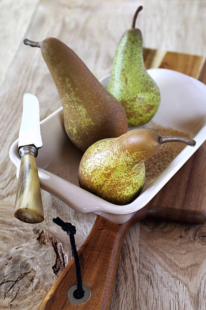 Three pears in baking dish, sugar and knife Three pears Conference in ceramic baking dish, brown sugar and vintage knife conference pear stock pictures, royalty-free photos & images