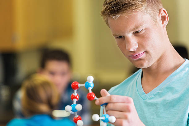 istock Caucasian teen boy studying plastic atom model in science class 473862866