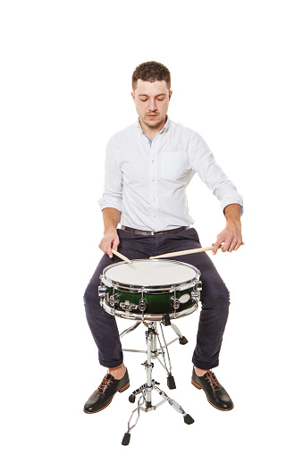 Handsome guy in a white shirt teaches properly play the drums on a white background