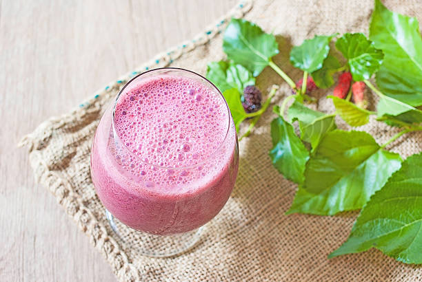 A glass of mulberry yogurt smoothie, a beautiful booster smoothie, on burlap and wood background.