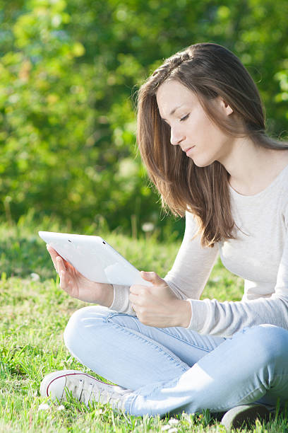 istock Young woman using tablet computer in park outdoors 473906678